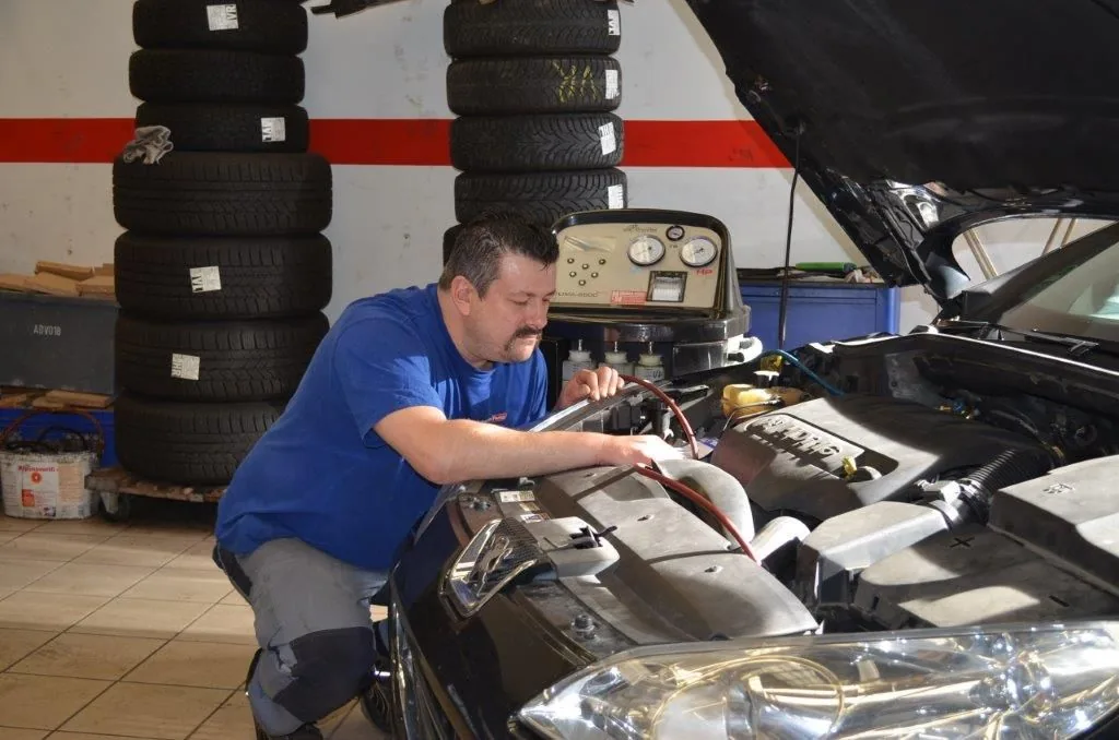 Klimaservicegerät steht am geöffneten Motorraum, ein Mitarbeiter schließt die Serviceschläuche an