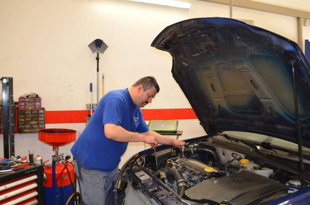 Kfz-Meister arbeitet mit einem Diagnosegerät am geöffneten Motorraum eines Fahrzeugs